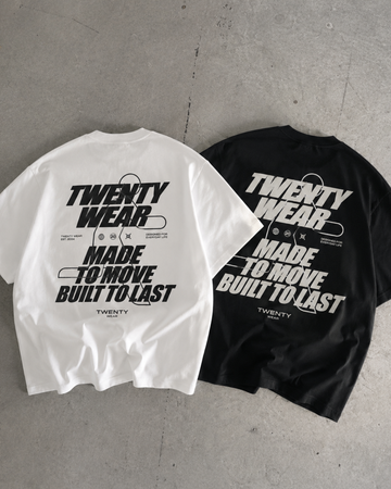 Two oversized short-sleeve T-shirts laid flat on a gray concrete floor, one white and one black, both featuring a large distressed graphic print that reads 'TWENTY WEAR MADE TO MOVE BUILT TO LAST' with small text below.