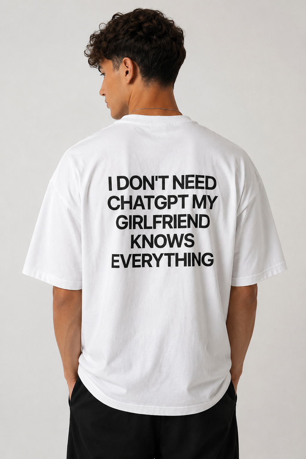 A man viewed from the back wearing a white t-shirt with bold black text that reads 'I DON'T NEED CHATGPT MY GIRLFRIEND KNOWS EVERYTHING'.